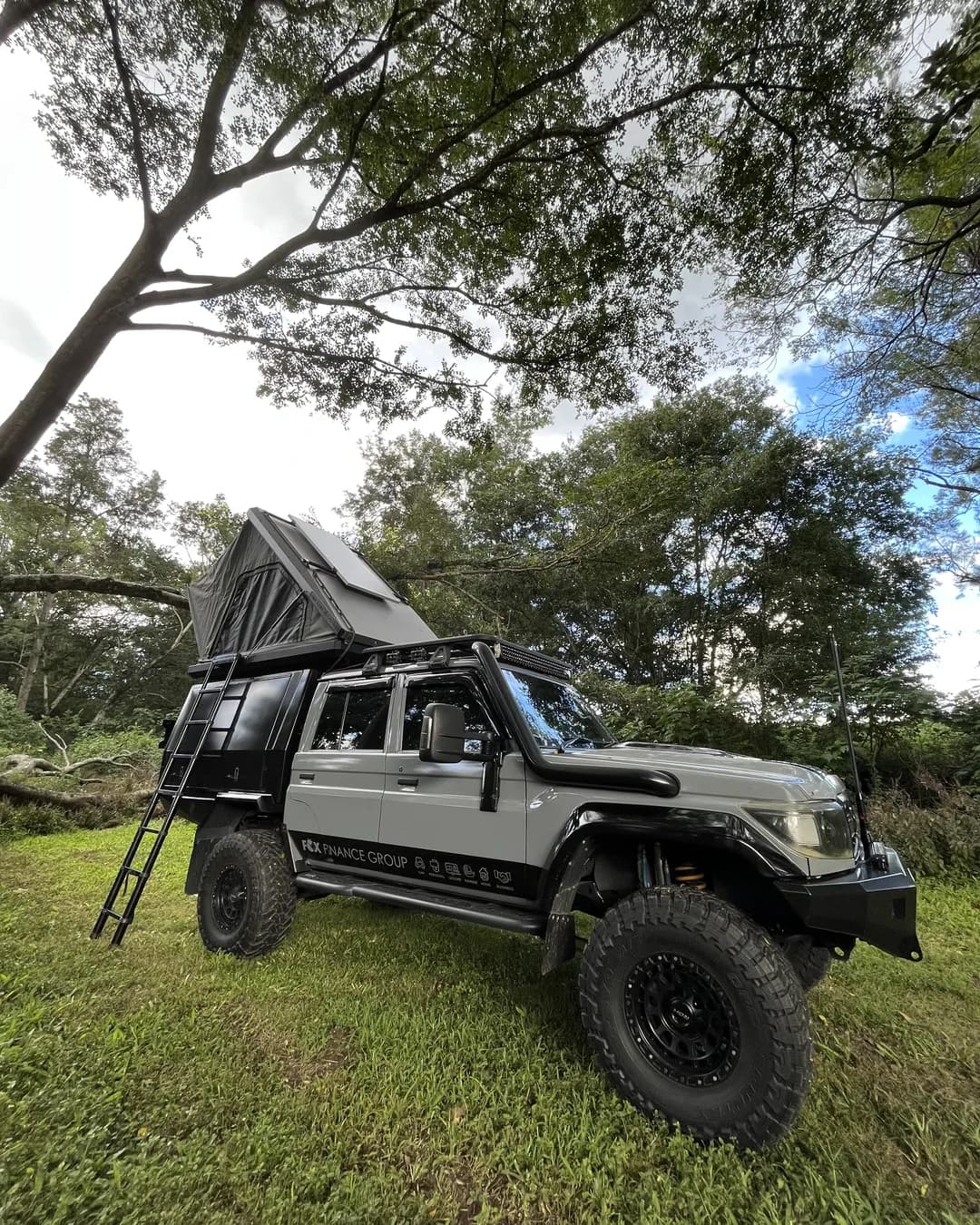 Drewsy's 79 set up under the trees, hard-shell rooftop tent open and the ladder down.