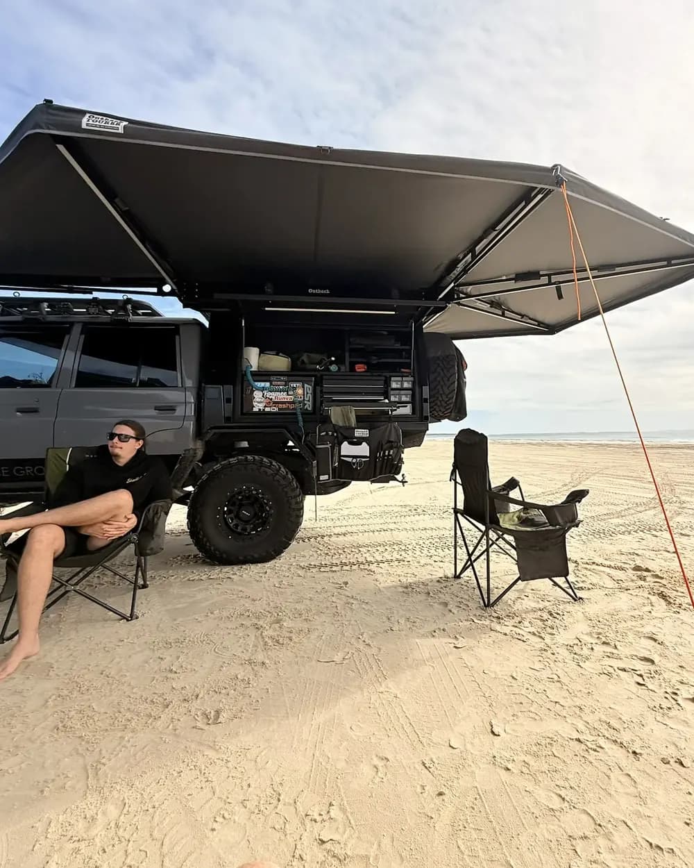 The canopy open under the awning on the beach, camp chairs set out.