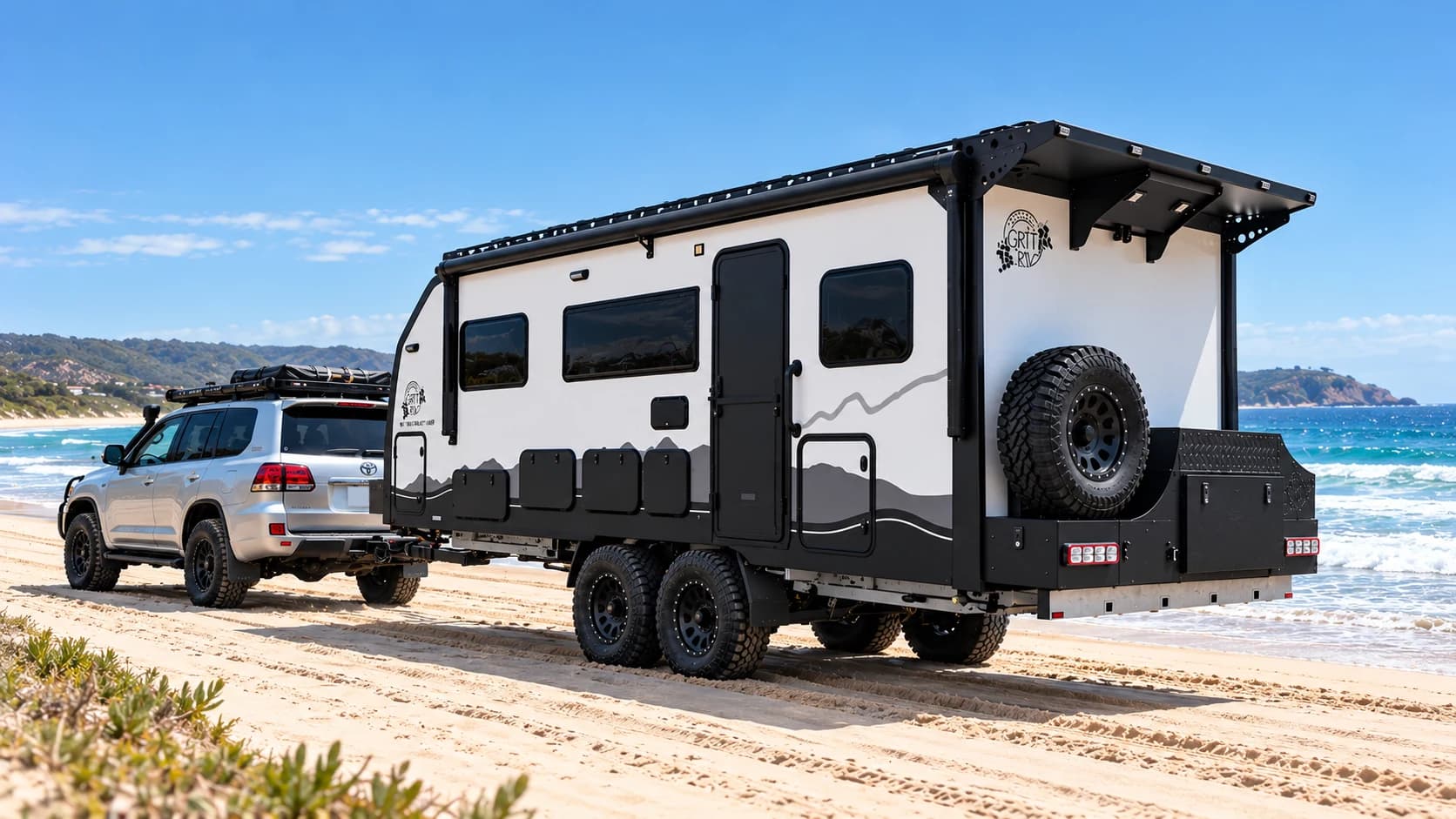 A silver 200 Series towing an off-road caravan along the beach, surf breaking behind.