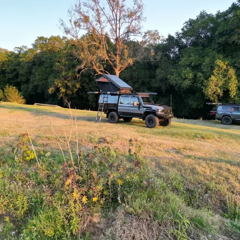 Drewsy's 79 camped in a grassy clearing at golden hour, rooftop tent up.